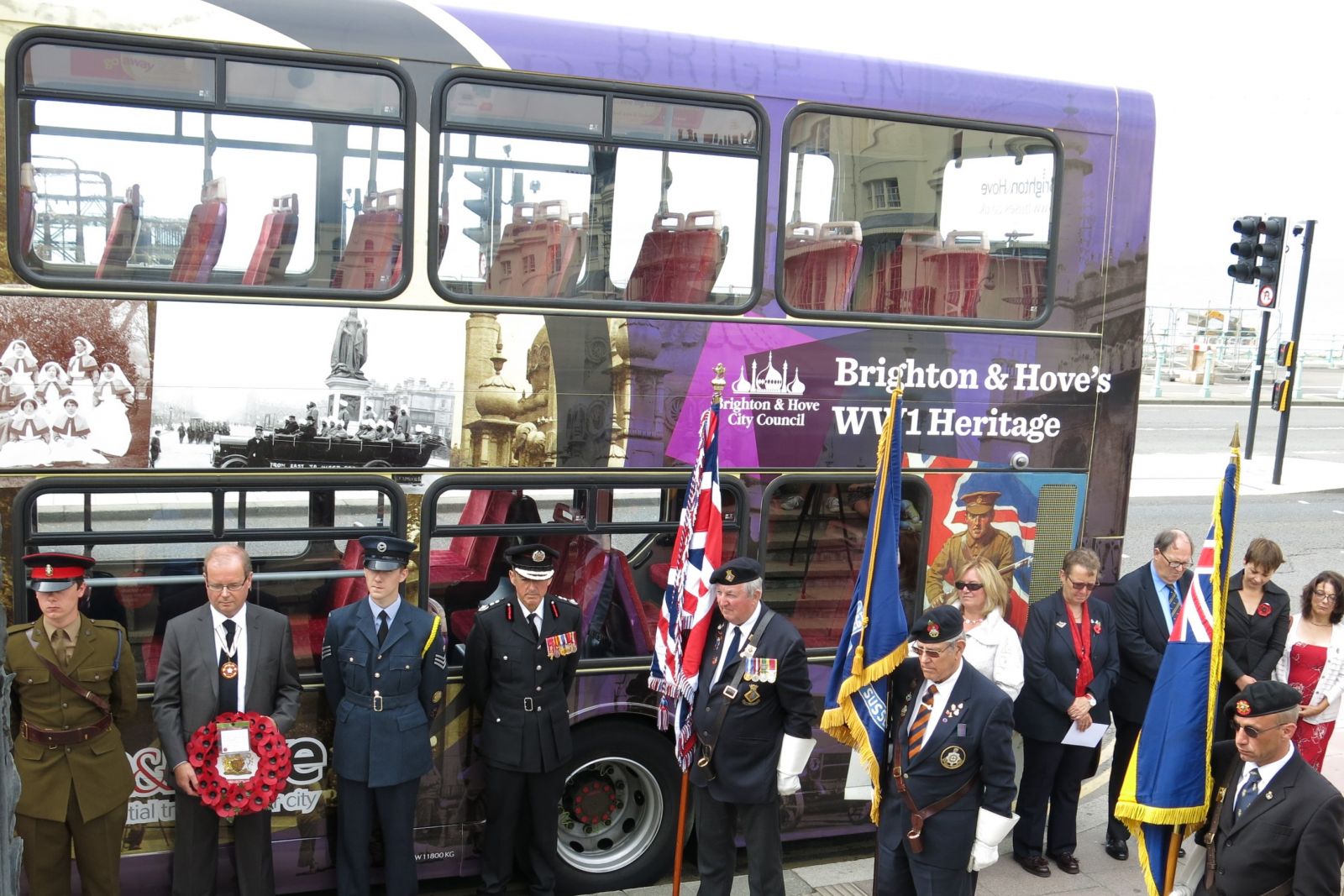 Photo of a bus decordated with photos of Brighton during WW1, a remebrance day parade stands in front of it